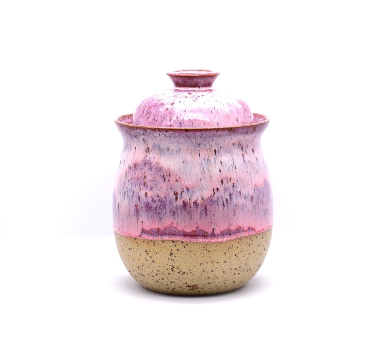 May include: A ceramic jar with a lid, featuring a speckled tan base and a body with a gradient of pink and purple hues. The jar has a rounded shape and a matching lid with a small knob.