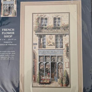 Könnte beinhalten: Kreuzstich-Set mit einer Darstellung eines französischen Blumengeschäfts. Das Bild zeigt ein Gebäude mit der Aufschrift "FLEURS PLANTES". Größe: 20 x 41 cm. Das Set enthält Baumwollgarn und 14-Count-Aida-Stoff.