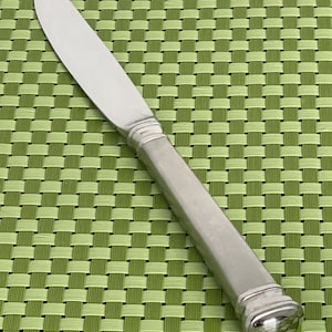 May include: A silver dinner knife with a rounded handle and a slightly curved blade.