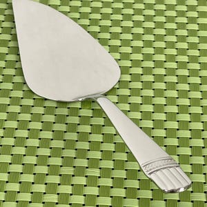 May include: A silver cake server with a decorative handle. The handle has a woven design and a raised edge.