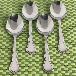 May include: Set of four silver soup spoons with ornate handles. The spoons are shiny and reflect light.