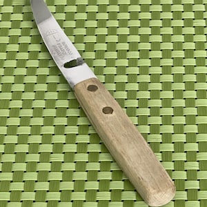 May include: A stainless steel paring knife with a wooden handle. The blade is silver and the handle is light brown, secured with two brass rivets. The knife has the text "ROWOCO FRANCE STAINLESS" etched on the blade.
