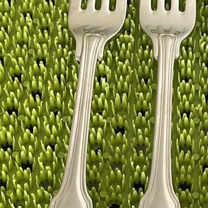 May include: Two silver forks with ornate shell-shaped handles, set against a green textured background.