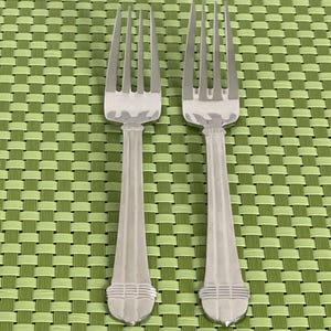 May include: Two silver forks with ornate handles on a green placemat.