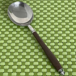 Peut inclure: Une cuillère de service en acier inoxydable avec un manche en bois brun foncé. La cuillère a un grand bol arrondi et une bande métallique argentée où le manche rencontre la cuillère. Le manche est cylindrique et se termine par une pointe décorative argentée.