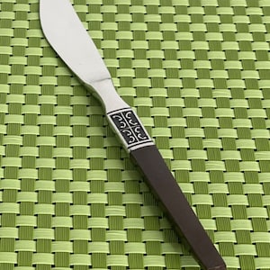 May include: A silver butter knife with a brown wooden handle. The handle has a decorative pattern of black swirls.