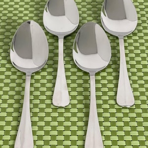May include: Four shiny, silver spoons with oval bowls and long, tapered handles. The spoons are arranged on a green and white checkered placemat, reflecting light. A classic set of silverware.
