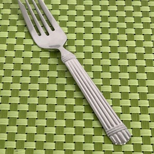 May include: A silver-toned metal fork featuring a three-pronged head and a handle with a vertical ribbed pattern. The handle design includes a horizontal band near the neck and a wider, rounded base with matching vertical grooves at the bottom end.