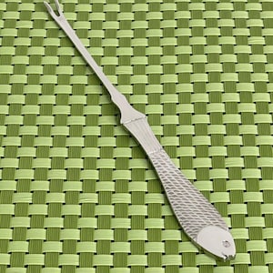May include: A silver fish-shaped fish bone remover with a pointed end and a forked end. The tool is designed to remove bones from fish.