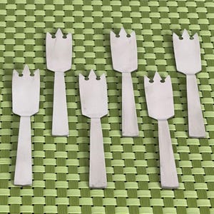 May include: Six silver-colored metal forks with a decorative tulip-shaped design. The forks are arranged in a row on a green and white checkered surface.
