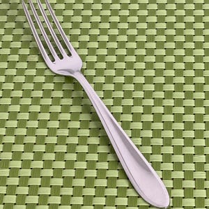 May include: A silver-coloured metal dinner fork with four long, slender tines and a smooth, tapered handle. The utensil features a polished, reflective finish and a simple, clean design with no decorative patterns or engravings on the surface.