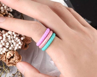 May include: Three silicone rings stacked on a finger. The rings are turquoise, pink and lavender.
