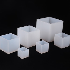 Peut inclure: Ensemble de six récipients translucides de forme carrée, de tailles variées. Les contenants ont un aspect givré et sont disposés sur un fond noir. Les ouvertures révèlent l'intérieur creux des cubes. Mesures en cm.