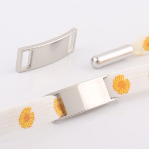 May include: White cotton ribbon with yellow daisy print and silver metal clasps. The ribbon has a silver metal slider that can be used to adjust the length.