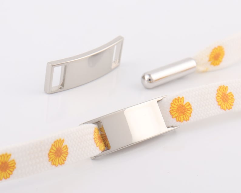 May include: White cotton ribbon with yellow daisy print and silver metal clasps. The ribbon has a silver metal slider that can be used to adjust the length.