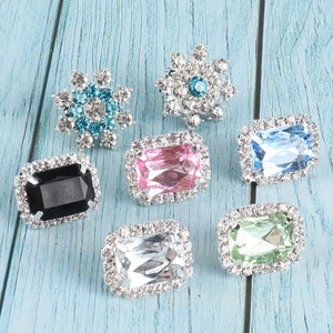 May include: Assortment of seven rhinestone embellishments in various shapes and colours.  The embellishments include a snowflake, a flower, and five rectangular shapes with different coloured rhinestones.