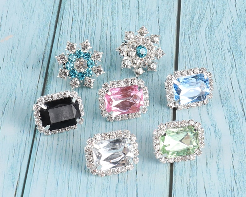 May include: Assortment of seven rhinestone embellishments in various shapes and colours.  The embellishments include a snowflake, a flower, and five rectangular shapes with different coloured rhinestones.