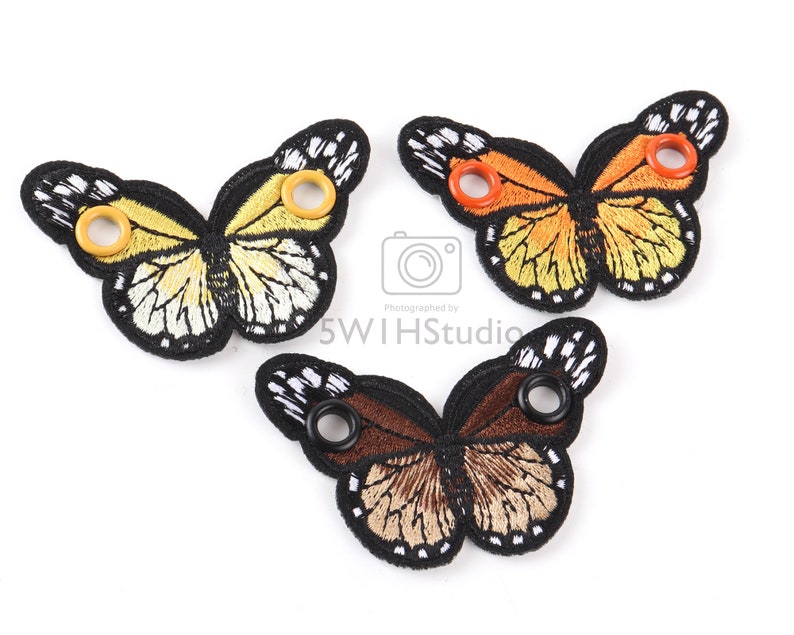 May include: Three embroidered butterfly shoe charms with black outlines and colorful wings. The butterflies have yellow, orange, and brown wings with black and white accents. Each butterfly has two eyelets for attaching to shoes.
