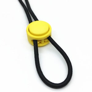 Puede incluir: Un bot&oacute;n redondo de pl&aacute;stico amarillo en un cord&oacute;n el&aacute;stico negro.