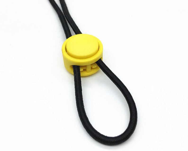 Puede incluir: Un bot&oacute;n redondo de pl&aacute;stico amarillo en un cord&oacute;n el&aacute;stico negro.