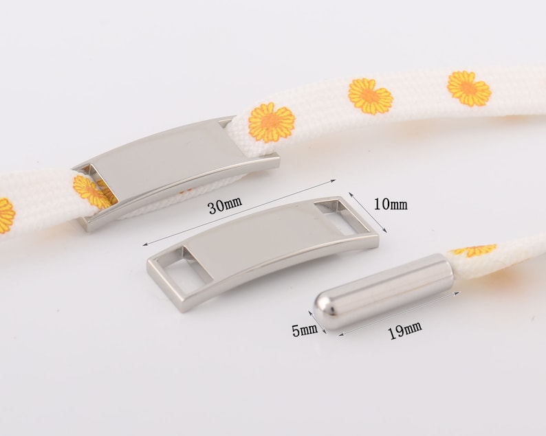 May include: Two silver metal tags with a rounded rectangular shape and a small hole for a string. The larger tag is 30 mm long and 10 mm wide. The smaller tag is 19 mm long and 5 mm wide.