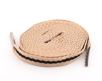 Könnte beinhalten: Ein Paar beige Schnürsenkel mit schwarzen Streifen. Die Schnürsenkel sind aufgerollt und einsatzbereit.