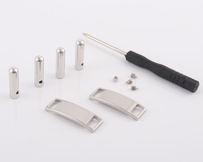 May include: A set of silver shoe charms with a blank space for engraving, a screwdriver, and four screws.