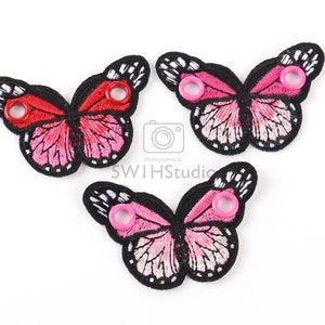 May include: Three pink and red butterfly shoe charms with black outlines and white accents. Each charm has a metal eyelet for attaching to a shoe.