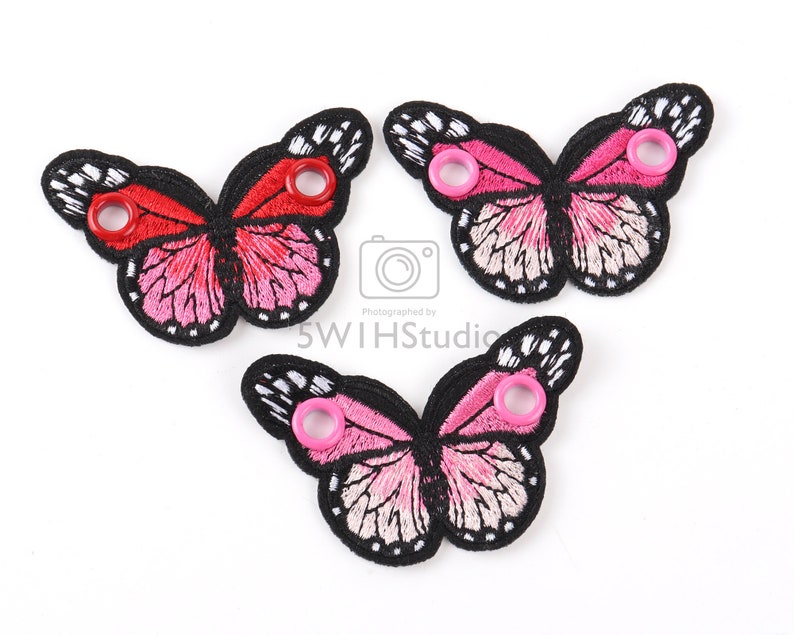 May include: Three pink and red butterfly shoe charms with black outlines and white accents. Each charm has a metal eyelet for attaching to a shoe.