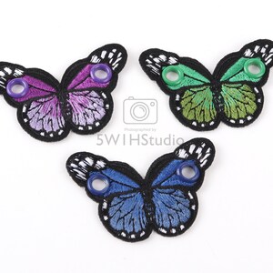 May include: Three embroidered butterfly shoe charms in purple, green, and blue with black outlines and white accents. Each charm has two eyelets.