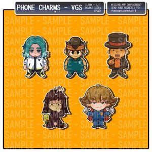 May include: Five colourful phone charms featuring cartoon characters. The charms are 1.4 inches in diameter and are double-sided. The characters are a green-haired boy in a white and black outfit, a boy with brown hair in a green and white outfit, a boy with brown hair in a black and orange outfit, a girl with brown hair in a black and purple outfit, and a boy with brown hair in a blue and red outfit.
