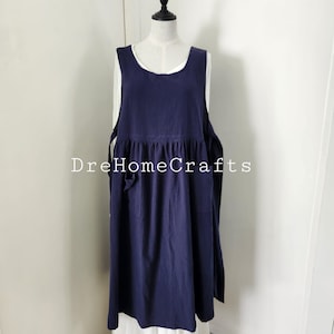 May include: A navy blue linen apron with a gathered skirt and two pockets. The apron is on a white mannequin and has a white background.