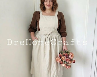 Puede incluir: Una blusa marrón de manga larga debajo de un delantal tipo pichi color crema con lazo en la cintura. El delantal tiene una falda amplia y el texto DreHomeCrafts está superpuesto en el centro. Se combina con un ramo de rosas rosas y melocotón.