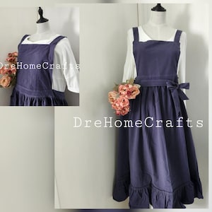 May include: A navy blue apron with a square neckline and ruffled hem, displayed on a mannequin. The apron has a waist tie and is layered over a white blouse. The text "DreHomeCrafts" is visible.