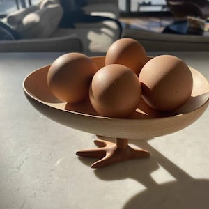 May include: A wooden bowl with four brown eggs inside. The bowl has a unique design with two legs that resemble chicken feet.
