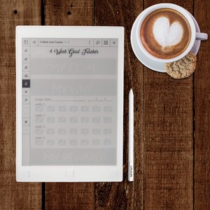Pu&ograve; includere: Un e-reader bianco con un modello di tracciamento degli obiettivi di 4 settimane visualizzato sullo schermo. Il modello include sezioni per "Il mio obiettivo", "Il mio perch&eacute;" e "La mia ricompensa". Ci sono caselle di controllo per ogni settimana del mese. L'e-reader &egrave; su una superficie di legno con una tazza di caff&egrave; e un biscotto.