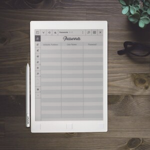 Pu&ograve; includere: Un e-reader bianco con uno schermo grigio che mostra un registro di password. Lo schermo ha colonne per l'indirizzo del sito web, il nome utente e la password. L'e-reader &egrave; su una superficie di legno con uno stilo bianco e un paio di occhiali.