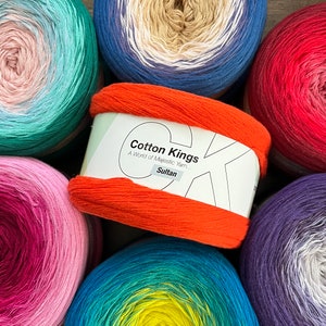 May include: A collection of colorful yarn skeins, including teal, blue, red, purple, orange, and yellow. The orange skein has a label that reads "Cotton Kings, A World of Majestic Yarn... Sultan".