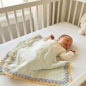 Può includere: Una coperta per neonati a righe verde chiaro con un bordo decorativo all'uncinetto in tonalità alternate di giallo, lavanda e verde menta. La coperta copre un neonato addormentato che indossa una maglia color crema a maniche lunghe.