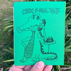 May include: A green booklet with the title "CROC-O-DIAL" and the text "Quick Facts About The Crocodilian Family". The cover features a cartoon illustration of a crocodile on the phone.