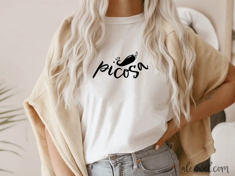 May include: White t-shirt with a black graphic of a chili pepper and the word "picosa" in a handwritten font.