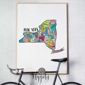 May include: A colorful map of New York State with each county labeled. The map is printed on white paper and framed in a light wood frame. The map is hanging on a white wall.