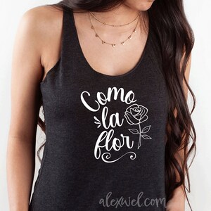 May include: A black tank top with a white graphic that says "Como la flor" with a stylized rose illustration. The text is in a cursive font.