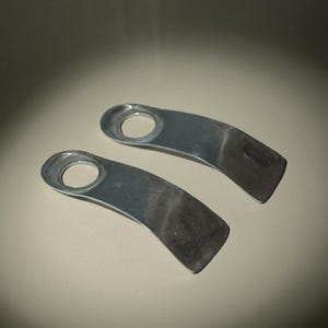 May include: Two silver-colored metal handles with a curved design and a circular opening at one end. The handles have a smooth, reflective surface and a slightly angled shape. The items are likely for a cabinet or drawer.