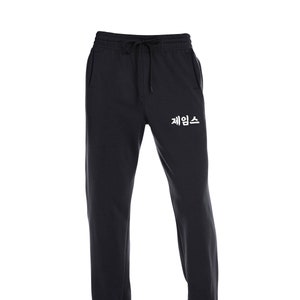 May include: Black sweatpants with a drawstring waist and a pocket on each side. The sweatpants have the Korean word "제임스" printed in white on the left leg.