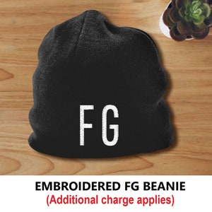 Puede incluir: Gorro negro con las letras blancas "FG" bordadas en la parte delantera. El gorro se muestra sobre una superficie de madera. El texto "EMBROIDERED FG BEANIE" est&aacute; debajo.