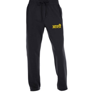 May include: Black sweatpants with a drawstring waist and a pocket on each side. The sweatpants have the word "आशी" embroidered on the left leg in yellow.