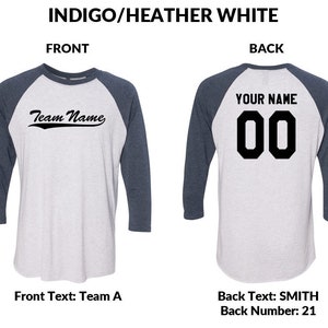 May include: A baseball jersey in a white and indigo blue colour scheme. The front of the jersey has the text "Team Name" in a black cursive font. The back of the jersey has the text "YOUR NAME" in black block letters above the number "00" in black block letters.
