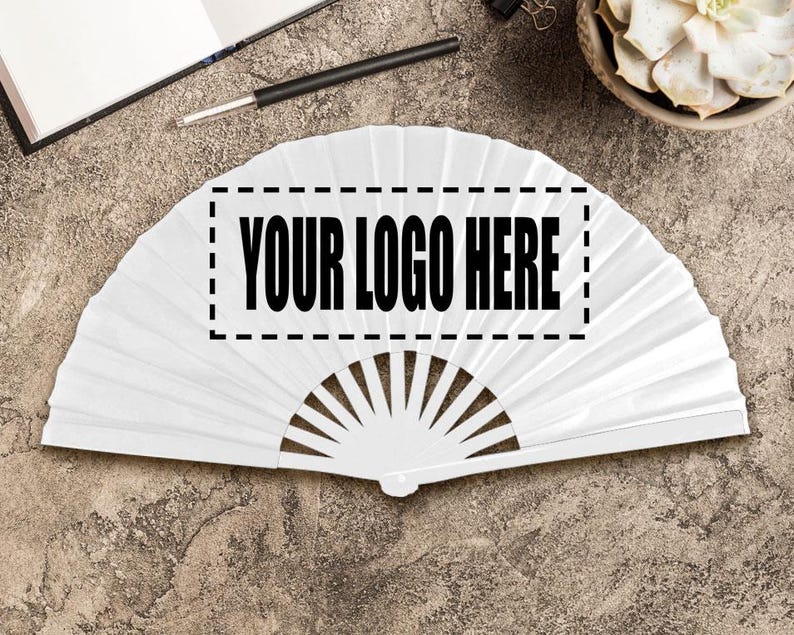 May include: A white folding fan with a semi-circular shape. The fan has a rectangular area with the text "YOUR LOGO HERE" in bold, black letters. The fan is lying on a textured, grey surface.