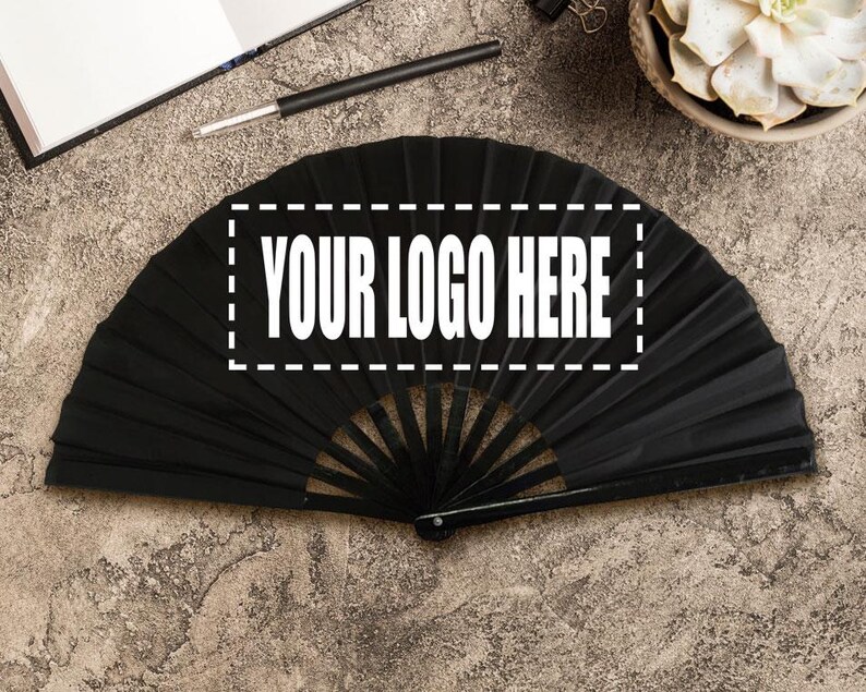 May include: A black folding fan with the text "YOUR LOGO HERE" in a white rectangle. The fan is open, showing its pleated design. The background is a textured, neutral surface.